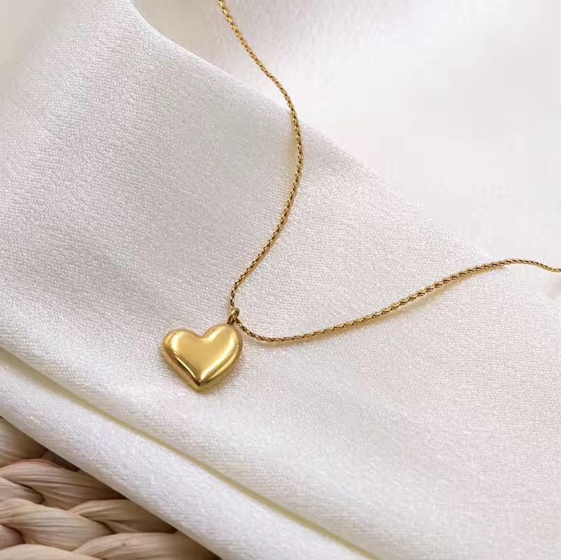 Gold heart pendant necklace on a delicate chain displayed on white satin fabric