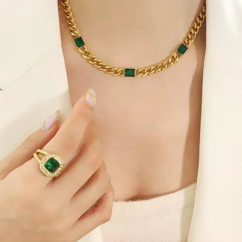 Gold chain necklace with green stone accents and matching gold ring with green gemstone