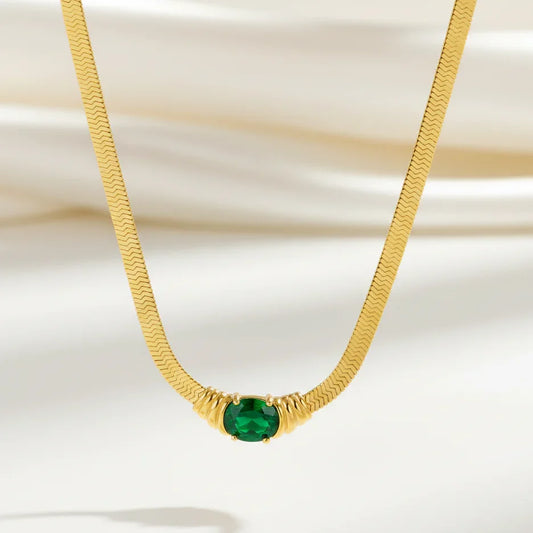 Gold chain necklace with green gemstone pendant on a soft white background