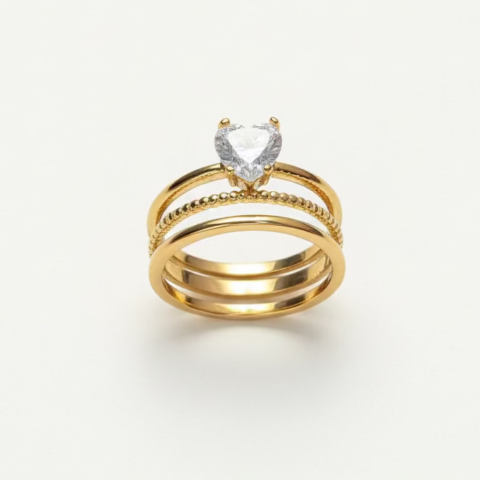 Stacked gold rings with heart-shaped gemstone centerpiece on a white background
