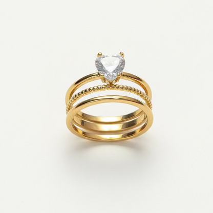 Stacked gold rings with heart-shaped gemstone centerpiece on a white background