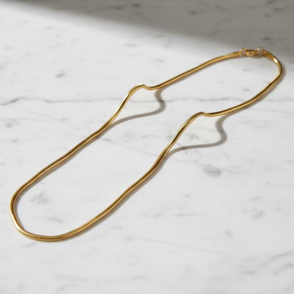 Gold snake chain necklace on white marble surface, minimalist anti-tarnish jewelry