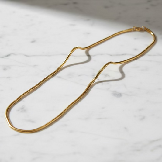 Gold snake chain necklace on white marble surface, minimalist anti-tarnish jewelry