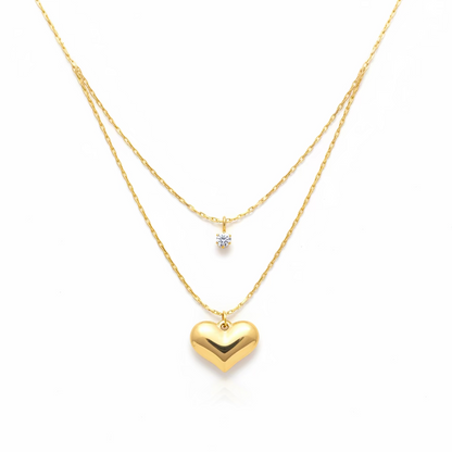 Layered gold necklace with heart pendant and small gemstone charm on white background