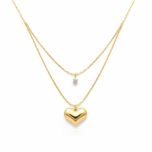 Layered gold necklace with heart pendant and small gemstone charm on white background