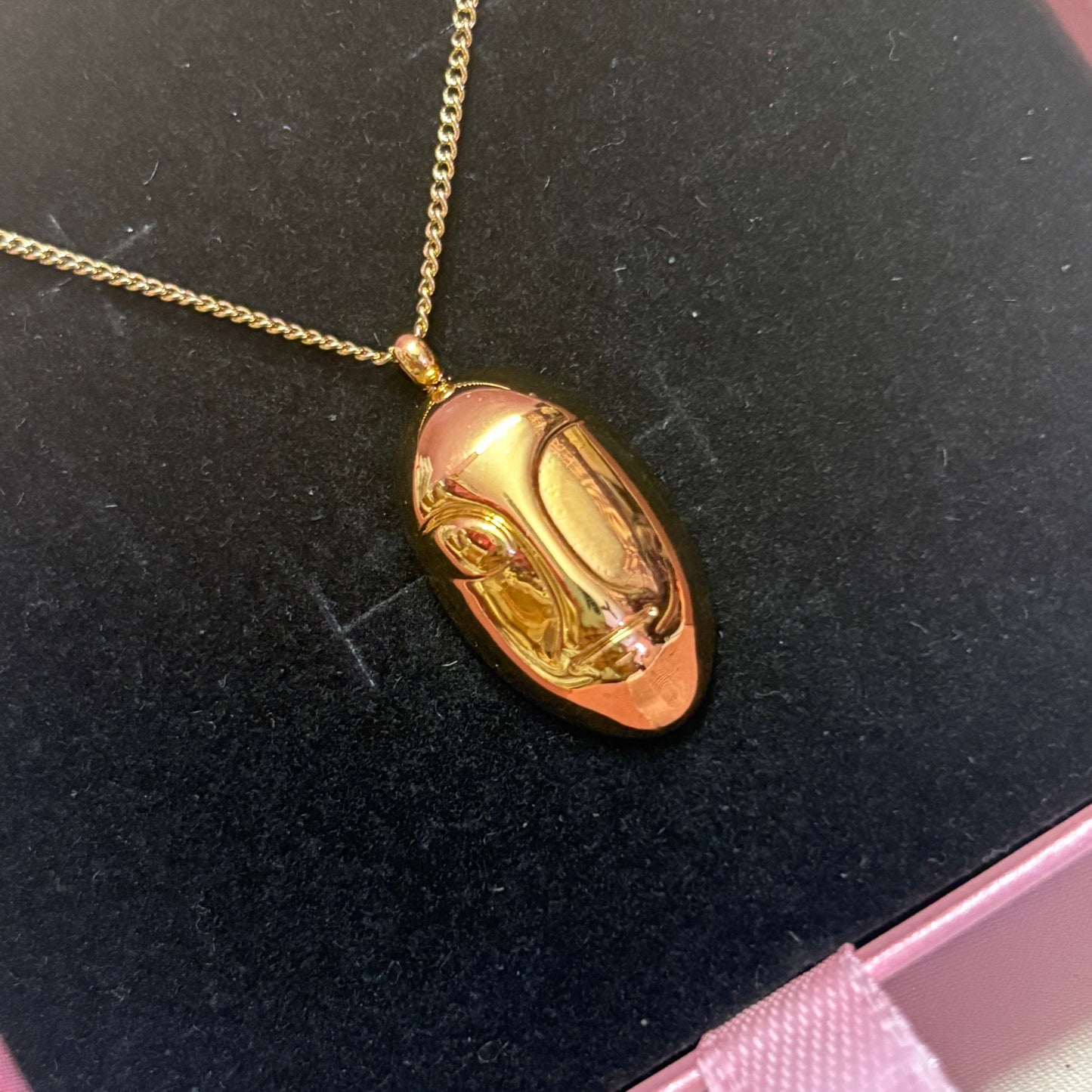 Gold face pendant necklace on a black velvet jewelry box