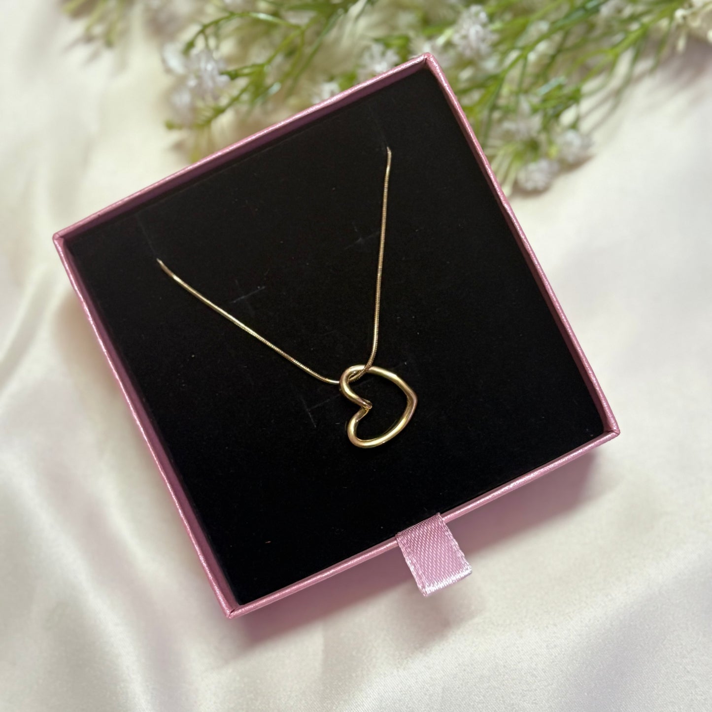 Gold heart pendant necklace in a pink jewelry box on satin with flowers