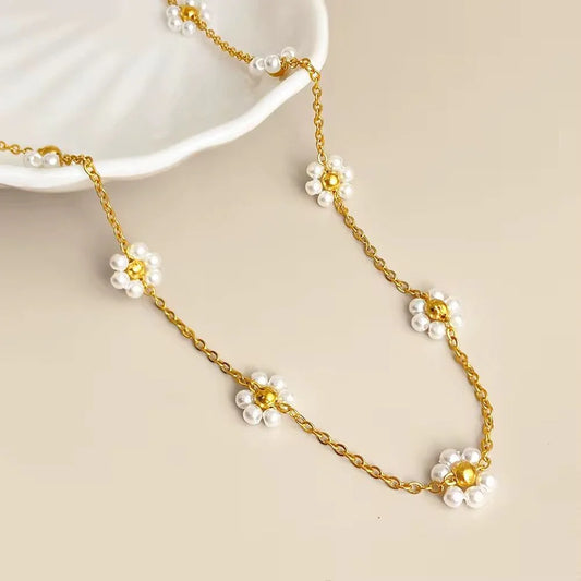 Gold chain necklace with white pearl daisy flower accents on neutral background
