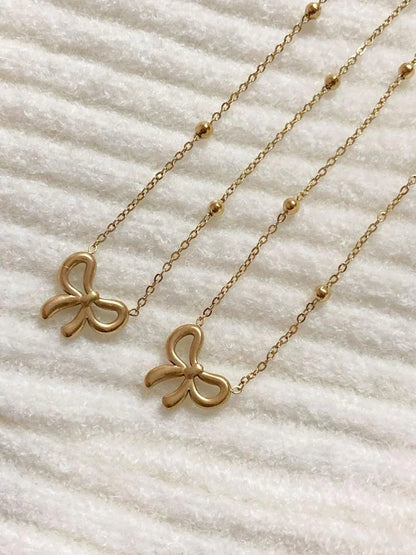 Gold bow pendant necklaces with delicate chains and bead accents on a white textured surface